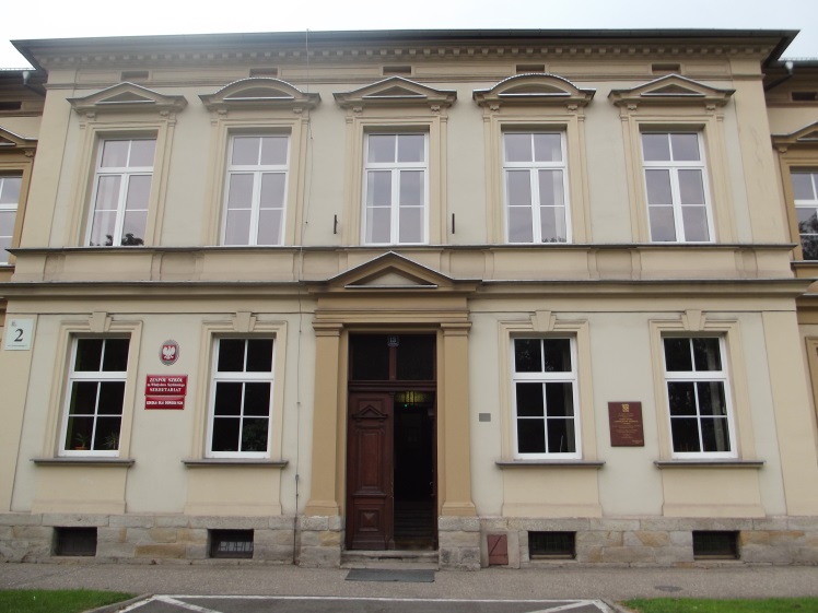 Dwukondygnacyjny budynek z symetryczną fasadą. Elewacja jasna z prostokątnymi oknami. Centralnie umieszczone drzwi wejściowe. Po lewej stronie tablice urzędowe. Budynek oznaczony numerem 2.