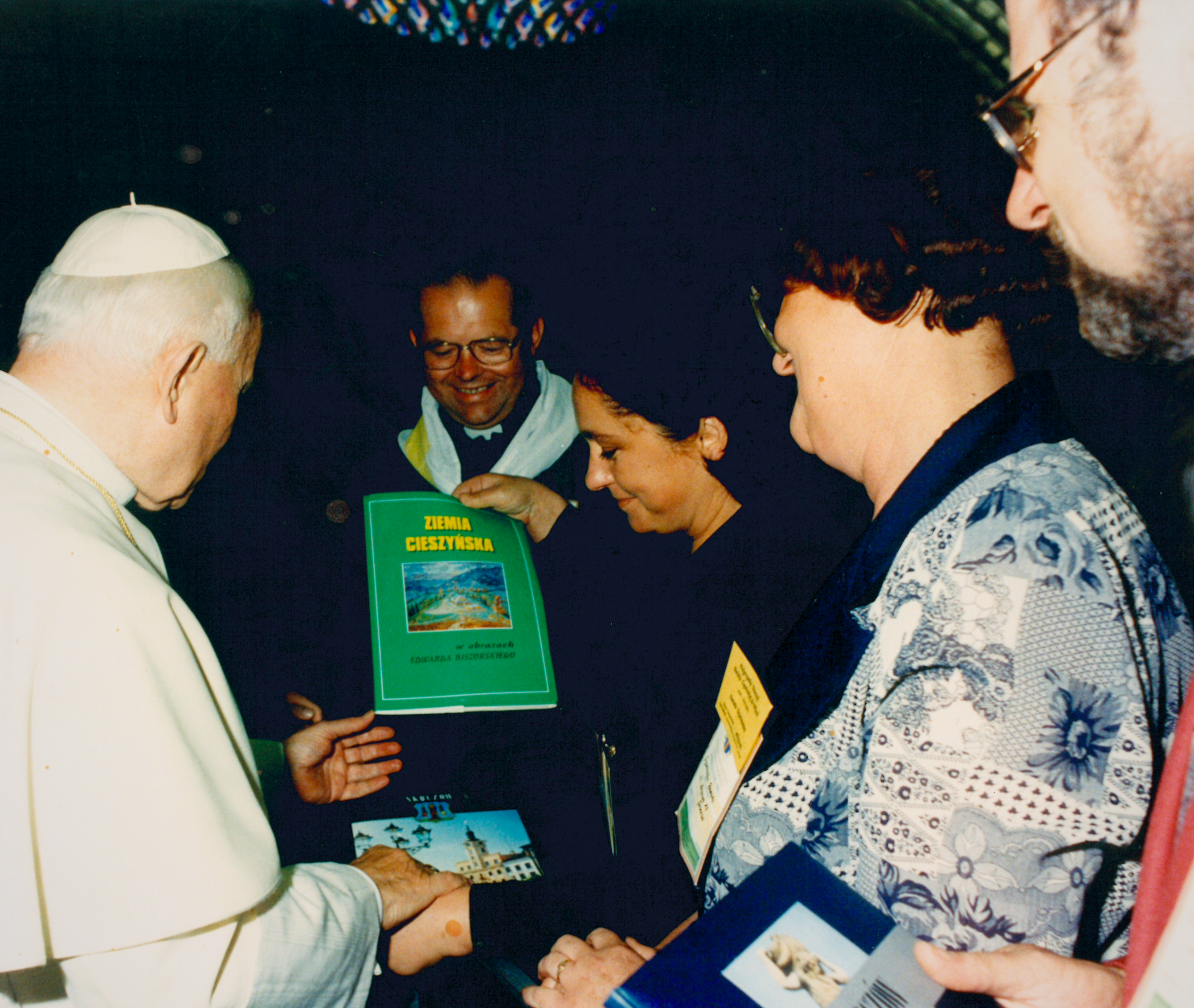 Papież Jan Paweł II spotyka się z grupą os&oacute;b (w środku Janina Żagan, obecna Starosta), kt&oacute;re wręczają mu albumy, w tym zielony pt. &bdquo;Ziemia Cieszyńska&rdquo;. Wszyscy uśmiechnięci, ujęcie pełne szacunku i serdeczności, z symboliczną wymianą pamiątek i książek.