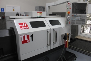 Tokarka CNC marki Haas model TL-1 w nowoczesnej pracowni; widoczne panele sterujące i okno z widokiem na drzewa.