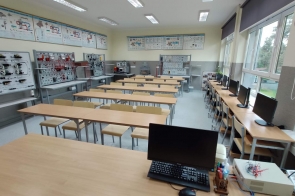Sala dydaktyczna z komputerami ustawionymi przy oknach; w centralnej części rzędy ławek, na ścianach tablice dydaktyczne z układami elektrycznymi - sala ZSTiO w Skoczowie.