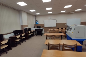 Sala dydaktyczna z rzutnikiem, tablicą, rzędami ławek oraz komputerami po lewej stronie; po prawej urządzenie techniczne, prawdopodobnie tokarka CNC - sala w ZST w Ustroniu.
