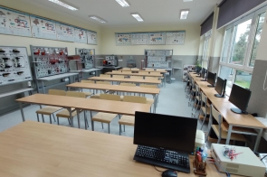 Sala dydaktyczna w Zespole Szkół Technicznych i ogólnokształcących w Skoczowie z długimi stołami i stanowiskami komputerowymi przy oknach. Na ścianach tablice edukacyjne i schematy techniczne.
