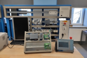 Stanowisko dydaktyczne z modułami automatyki przemysłowej, panelem HMI, sterownikiem PLC i komputerem. W tle okno i kaloryfer w Zespole Szkół Technicznych w Cieszynie.