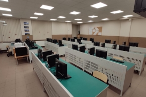 Sala komputerowa z kilkoma rzędami stanowisk wyposażonych w monitory, klawiatury i fotele. Na ścianie zegar i tablica korkowa w Zespole Szkół Technicznych w Ustroniu.
