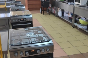 Sala gastronomiczna z kuchenkami i piekarnikami w rzędzie. Po prawej stronie blat roboczy z kuchennym wyposażeniem i szafkami wiszącymi w Zespole Placówek-Szkolno-Wychowawczo-Rewalidacyjnych w Cieszynie.