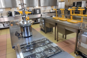 Stanowisko kuchenne z płytą gazową i fontanną czekoladową. W tle zlewy, żółte krzesła na blatach i stalowe szafki kuchenne w Zespole Placówek Szkolno-Wychowawczo-Rewalidacyjnych w Cieszynie.