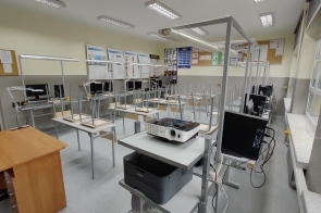 Sala komputerowa z kilkunastoma stanowiskami wyposażonymi w monitory, klawiatury i sprzęt elektroniczny, ustawionymi w rzędach. Na pierwszym planie biurko z rzutnikiem w Zespole Szkół Technicznych i Ogólnokształcących w Skoczowie.