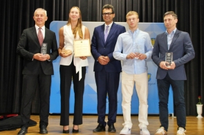 Pięć osób stoi na scenie podczas Gali Sportu. Czworo z nich trzyma w rękach statuetki i dyplomy. W tle widoczne jest logo Powiatu Cieszyńskiego na niebieskim tle.