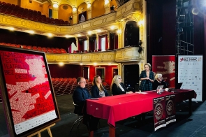 Pusta widownia czerwonych foteli w zabytkowym teatrze, na scenie przy długim stole z bordowym obrusem siedzi kilku prelegentów, jedna kobieta stoi i przemawia. Z lewej duży plakat „34. Międzynarodowy Festiwal Teatralny Bez Granic” na sztaludze, po prawej roll-upy partnerów.