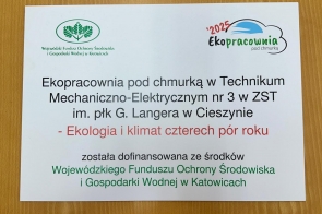Biała tablica informacyjna na drewnianym blacie z logotypami WFOŚiGW i „Ekopracownia 2025”. Tytuł projektu w ZST w Cieszynie: „Ekopracownia pod chmurką – Ekologia i klimat czterech pór roku”, z adnotacją o dofinansowaniu.