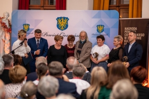 Grupa osób stoi na scenie przed publicznością podczas uroczystości. Część uczestników trzyma statuetki, a w tle widoczna jest ścianka.