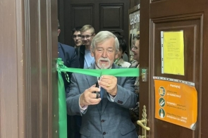 Stanisław Kubicius Przewodniczący Rady przecina zieloną wstęgę przy wejściu do sali. W tle widoczne są osoby stojące w pomieszczeniu, a na drzwiach znajdują się kartki informacyjne.