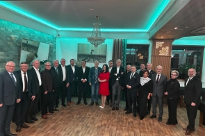 Grupa osób pozuje do zdjęcia w sali konferencyjnej. W tle widoczne są dekoracyjne oświetlenie, żyrandol, obrazy oraz turkusowe podświetlenie sufitu.