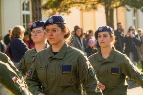 Uczniowie w mundurach stoją w szyku. Mają granatowe berety, a na mundurach widoczne są naszywki z polską flagą oraz oznaczenia klasy mundurowej.