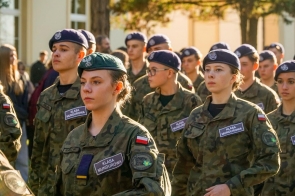 Uczniowie w mundurach stoją w zwartym szyku. Na mundurach widoczne są naszywki z polską flagą i napisem „Klasa mundurowa”, a część osób ma berety.