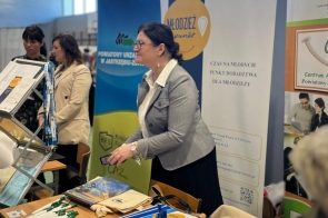  Przy stole z materiałami promocyjnymi stoi kobieta, a w tle widoczne są banery dotyczące doradztwa zawodowego i rynku pracy.