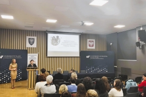 Przed publicznością stoją dwie osoby, a na ekranie wyświetlona jest prezentacja dotycząca budowania więzi i bliskości w rodzinie zastępczej i adopcyjnej.