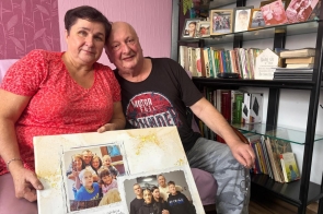Dwie osoby siedzą obok siebie w domowym wnętrzu. Trzymają pamiątkowy album ze zdjęciami rodzinnymi, a w tle widać regał z książkami i fotografiami.
