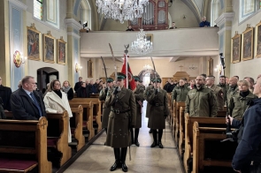 Wnętrze kościoła z ławkami po obu stronach. Przez nawę główną idą osoby, część w mundurach. W ławkach siedzą uczestnicy uroczystości. W tle ołtarz i dekoracje świątyni.
