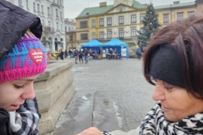 Janina Żagan Starosta Cieszyńska przypinająca czerwone serduszko na kurtce dziewczynki trzymającej puszkę do zbiórki, w tle rynek z ratuszem i świąteczną choinką. Starosta Cieszyńska wrzuca datek do puszki w Cieszynie.