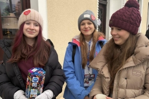 Trzy dziewczyny stojące na zewnątrz przy budynku, jedna trzyma puszkę do zbiórki, a pozostałe mają na sobie zimowe ubrania i czapki. Wolontariusze z Ustronia.