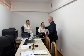 Dwie kobiety siedzące przy biurkach z laptopami wyciągają ręce do powitania Mieczysława Szczurka Wicestarosty Cieszyńskiego stojącego naprzeciwko; na stole widoczne dokumenty i akcesoria biurowe.