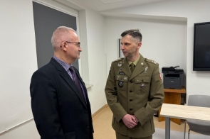 Dwóch mężczyzn prowadzących rozmowę w pomieszczeniu; jeden w garniturze Mieczysław Szczurek Wicestarosta Cieszyński, drugi w mundurze wojskowym z odznaczeniami.
