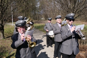 Orkiestra w mundurach gra na instrumentach dętych i werblu podczas uroczystości na świeżym powietrzu.