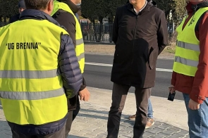 Czterech mężczyzn rozmawia przy drodze na nowym chodniku, dwóch z nich ma kamizelki odblaskowe z napisem „UG Brenna”.