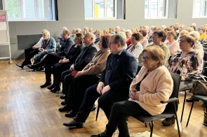 Grupa osób siedzi w rzędach i słucha prelekcji, wszyscy zwróceni w stronę prowadzącego.
