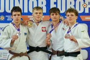 Czterech młodych mężczyzn w strojach judo stoi obok siebie, prezentując zdobyte medale. Jeden z nich ma na szyi złoty medal, pozostali trzymają swoje medale w dłoniach.