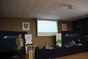 Prelegent, Jakub Skałka, przemawia podczas konferencji dla uczniów, w tle ekran z prezentacją.