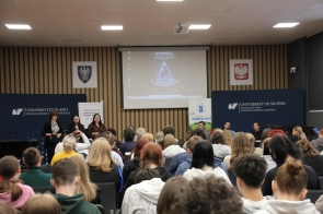 Uczniowie uczestniczą w konferencji, siedząc na krzesłach podczas prezentacji.
