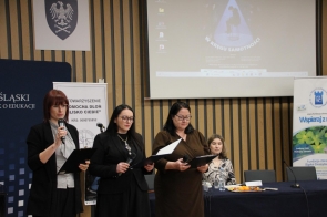 Trzy kobiety prowadzące konferencję stoją z mikrofonami, za nimi jest rzutnik z prezentacją.