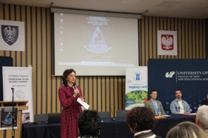Dziekan dr hab. Katarzyna Marcol - profesor Uniwersytetu trzyma mikrofon, w tle widoczna prezentacja. 