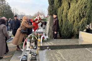 Kobieta składa bukiet kwiatów na grobie ozdobionym wieńcami i zniczami.