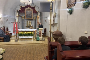 Wnętrze kościoła z ołtarzem udekorowanym kwiatami i świecami. Przy ambonie stoi mężczyzna, a w ławkach siedzą uczestnicy.