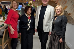 Cztery osoby stoją obok siebie w pomieszczeniu z ceglanym sklepieniem, w tle widać stół i innych ludzi.