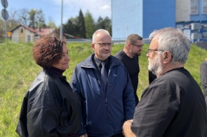 Janina Żagan Starosta Cieszyński stoi bokiem z lekkim uśmiechem, obok niej Mieczysław Szczurek Wicestarosta Cieszyński, oboje znajdują się wśród innych osób na zewnątrz.