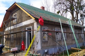 Budynek w trakcie remontu z rusztowaniami i odkrytą konstrukcją dachu, wokół którego znajdują się drabiny oraz materiały budowlane.