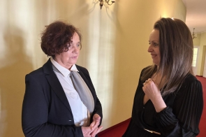 Janina Żagan Starosta Cieszyński stoi naprzeciwko Katarzyny Dendys-Koseckiej Dyrektor Teatru im. Adama Mickiewicza w Cieszynie, w korytarzu o jasnych ścianach i czerwonej podłodze, prowadząc rozmowę.