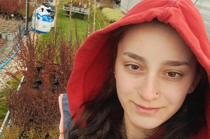 Młoda dziewczyna w czerwonej bluzie z kapturem robi selfie, wśród doniczek i tuneli foliowych.