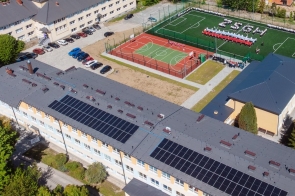 Widok z góry na teren szkoły z budynkami, parkingiem oraz boiskiem sportowym. Na boisku piłkarskim osoby tworzą napis „ZSGH”. Obok widoczne jest boisko wielofunkcyjne.