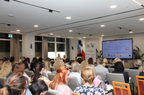 Uczestnicy konferencji siedzą w rzędach w sali i są zwróceni w stronę mównicy. Z przodu widoczna jest osoba przemawiająca, baner oraz duży ekran z prezentacją dotyczącą edukacji włączającej.