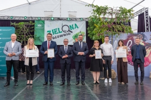 Grupa osób stoi na scenie podczas wydarzenia. Dwie osoby trzymają dyplomy i tablicę z napisem „Zielona Pracownia”. W tle widoczny jest baner wydarzenia oraz elementy scenografii.