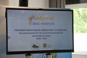 Na dużym ekranie w sali wyświetlona jest prezentacja programu „Aktywni bez metryki”. W tle widać okno z zielenią za szybą.