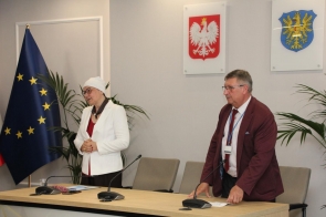 Dwie osoby stoją przy stole konferencyjnym w sali sesyjnej. Po lewej stronie znajduje się Anna Stefaniak-Bacza Dyrektor Powiatowego Urzędu Pracy w Cieszynie w białej marynarce, po prawej Jerzy Pilch Członek Zarządu w bordowej marynarce. 