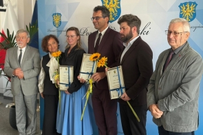 Grupa wyróżnionych osób pozuje do zdjęcia podczas gali sportu, trzymając dyplomy, statuetki i słoneczniki. 