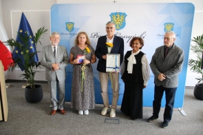 Grupa wyróżnionych osób pozuje do zdjęcia podczas gali sportu, trzymając dyplomy, statuetki i słoneczniki. 