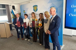 Grupa wyróżnionych osób pozuje do zdjęcia podczas gali sportu, trzymając dyplomy, statuetki i słoneczniki. 